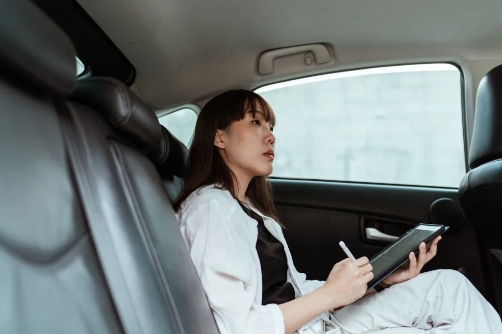 Woman in car backseat using tablet with stylus, illustrating travel-ready backseat organizer and leather seat storage