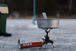 Portable single-burner butane camping stove with pot and fuel canister on icy ground