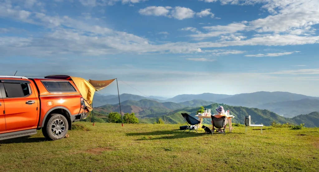 Foldable camping chair beside orange truck and picnic table on mountain overlook — road trip camping setup
