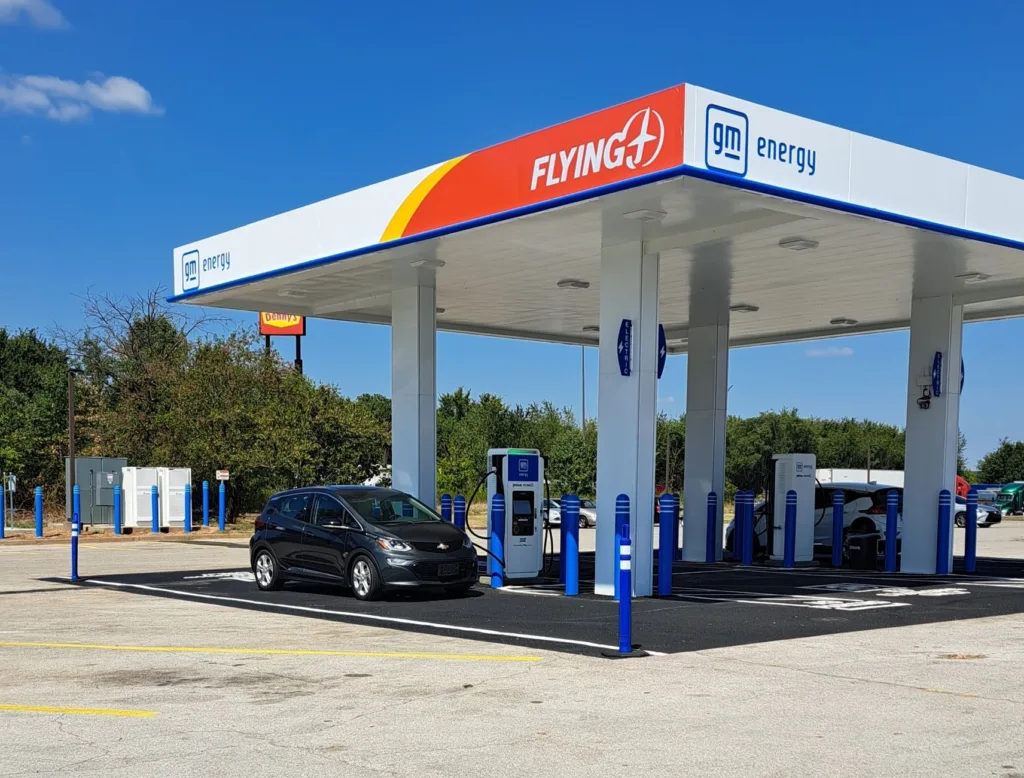 Chevy Bolt plugged into GM Energy EV charger under Flying A canopy at a multi-port charging station