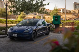 Blue Tesla plugged into green KVolt EV charger at a public station, demonstrating an EV charger for multiple vehicles