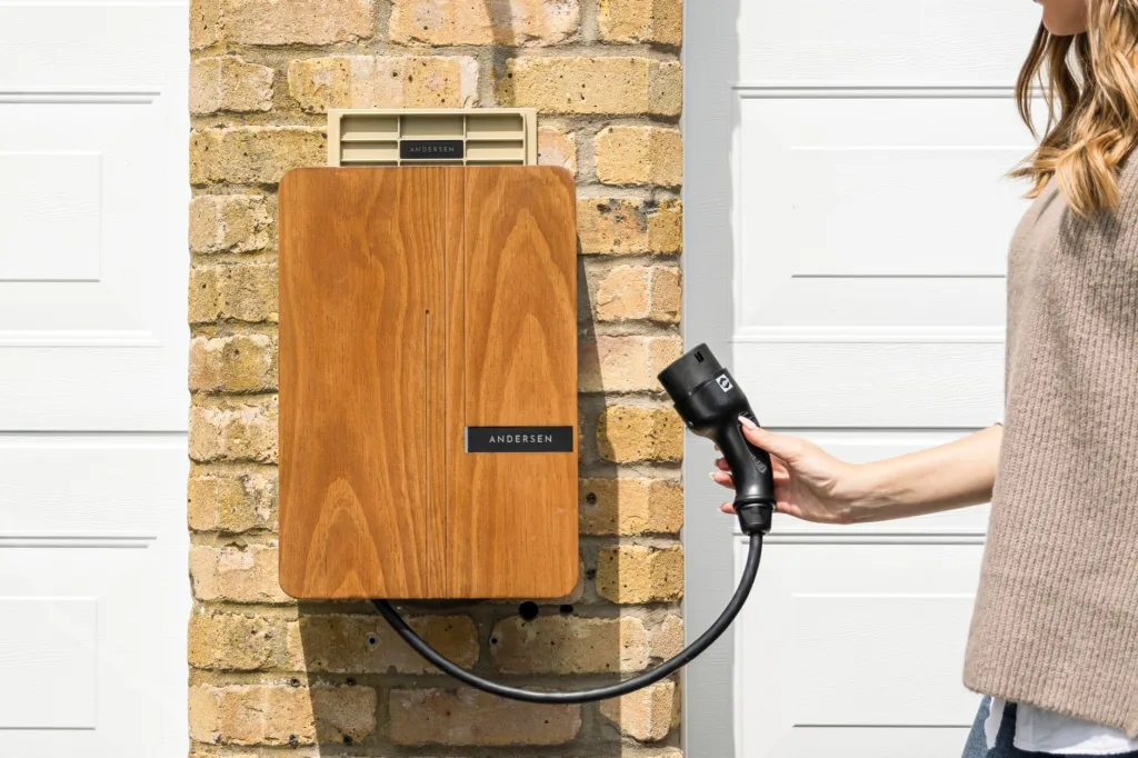 Wall-mounted EV charger with wooden faceplate and tethered charging cable on brick wall for outdoor installation