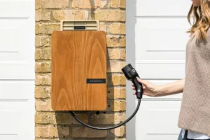 Wall-mounted EV charger with wooden faceplate and tethered charging cable on brick wall for outdoor installation