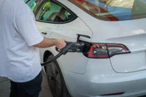 Person plugging an EV extension cord into a white electric car's level one charging port, EV charging cable connected