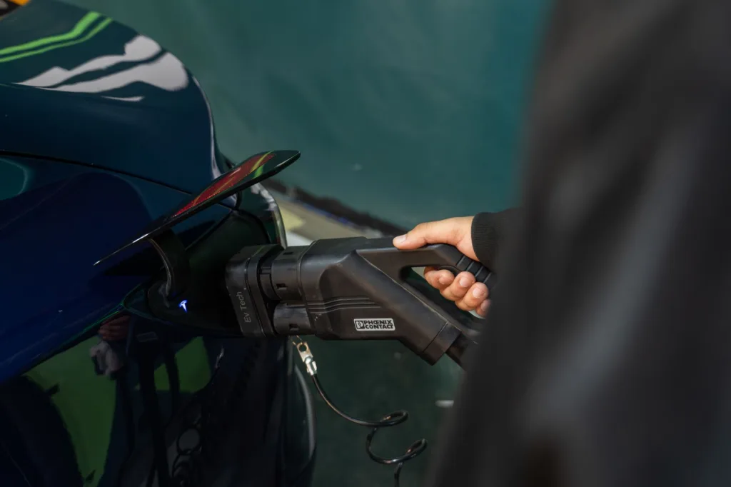 Hand inserting hardwired EV charger plug into electric vehicle charging port, close-up of connector and handle