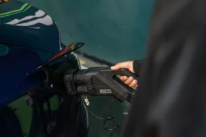 Hand inserting hardwired EV charger plug into electric vehicle charging port, close-up of connector and handle