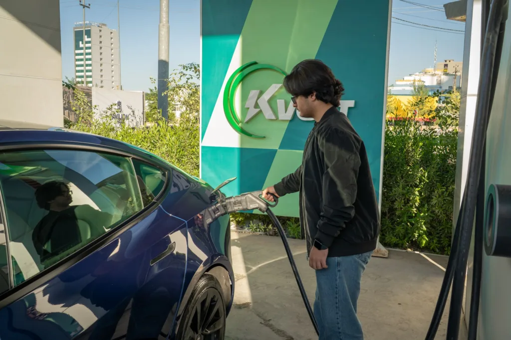 Person plugging a level two EV charger into a blue electric car at a home charging station