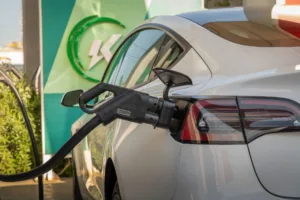 Smart EV charger plug connected to rear charging port of a white electric car at a charging station