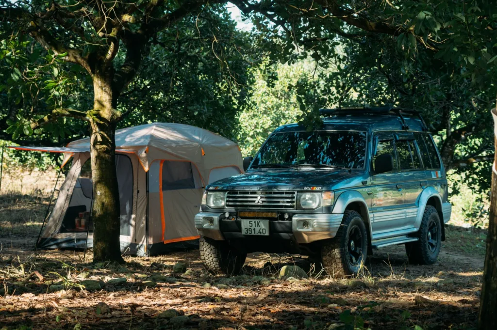 Blue SUV parked next to a spacious SUV camping tent under trees at a shaded campsite