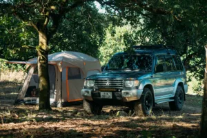 Blue SUV parked next to a spacious SUV camping tent under trees at a shaded campsite