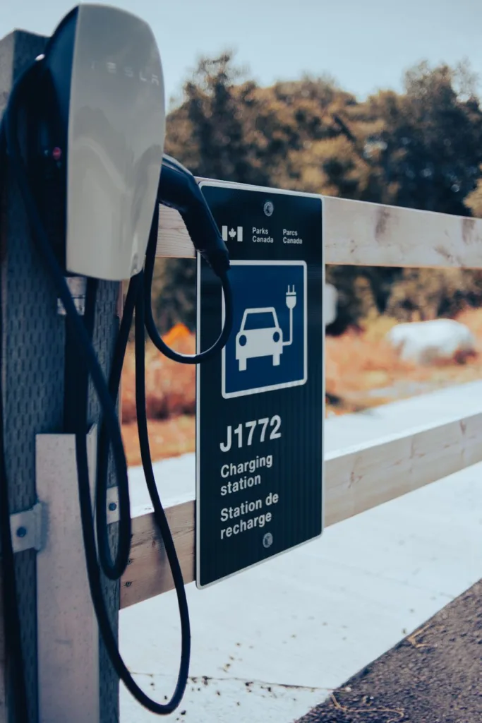 Tesla wall charger and cable beside a J-type charging station sign, illustrating Tesla to J adapter use