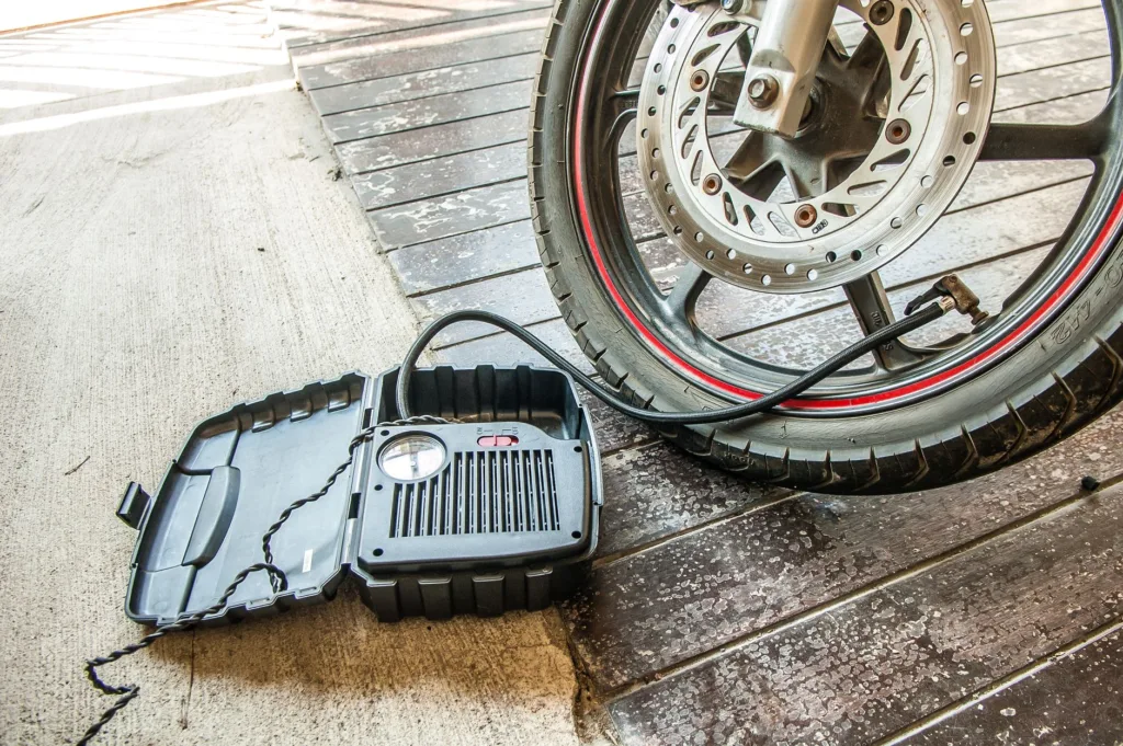 Portable tire inflator with pressure gauge connected to motorcycle wheel on pavement — compact air compressor for road trips