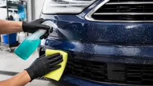 Bug remover spray and microfiber cloth cleaning residue from a dark car bumper
