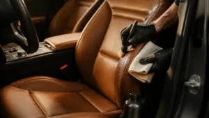 Detailing brush and microfiber cloth cleaning a tan leather car seat
