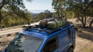 Blue camper van with bicycle surfboard and luggage secured on a roof rack
